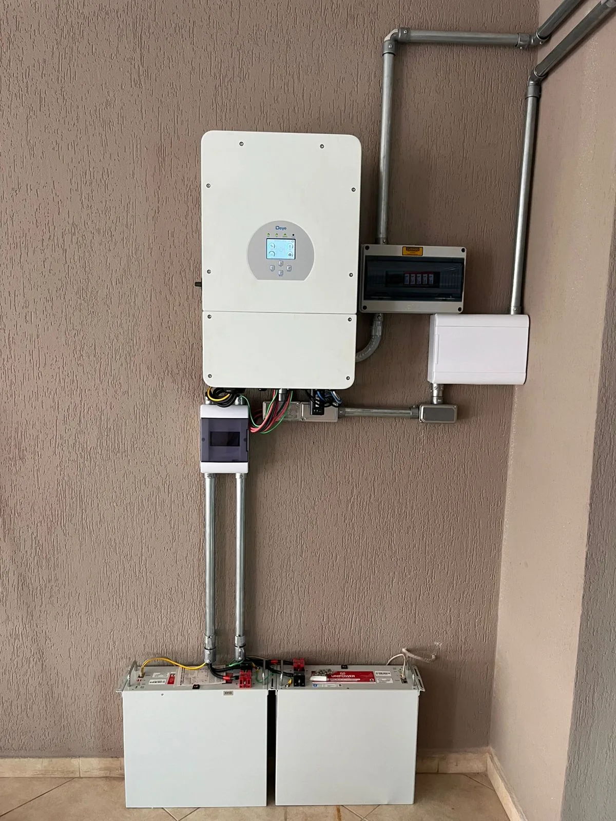Inversor híbrido Deye instalado na parede ao lado do banco de baterias de um sistema solar residencial